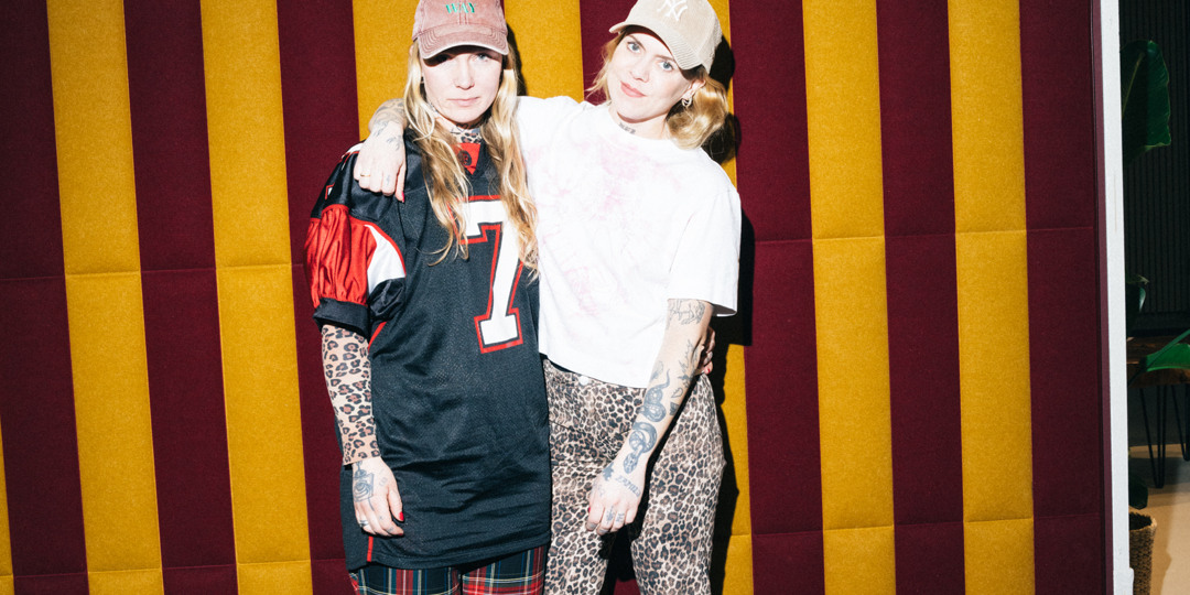 SFF25_martinbrusewitz_lores-40.jpg two young women visiting the fair 2025, posing for the camera. The backwall is striped in red and yellow.
